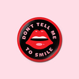 Button with the text "Don't tell me to smile" surrounding an illustration of lips.