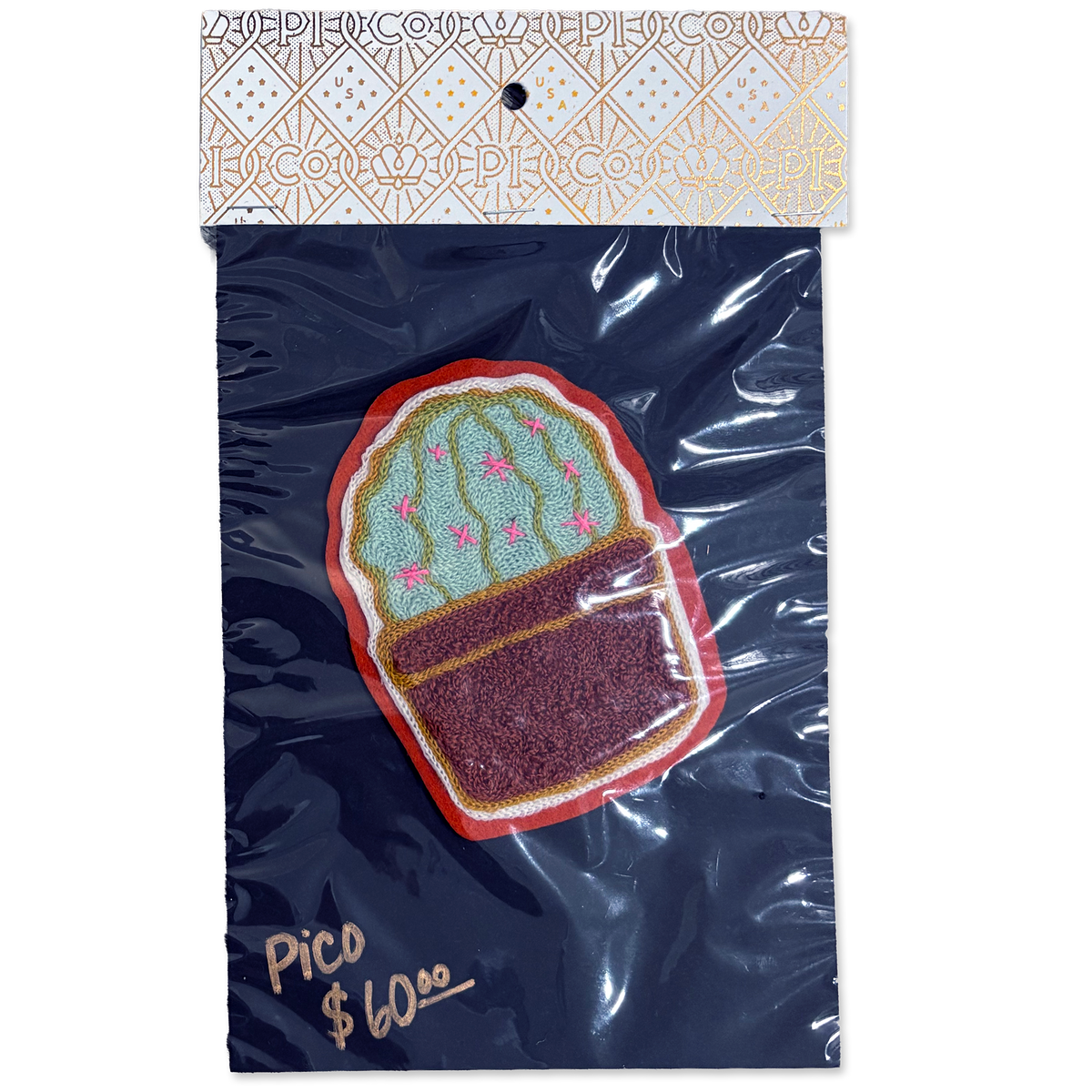 An embroidered cactus patch in a pot, packaged in a clear plastic bag with a branded header card. The patch features a green cactus with pink details and a dark brown pot, set against a dark navy blue backing card with gold foil text and a patterned top.