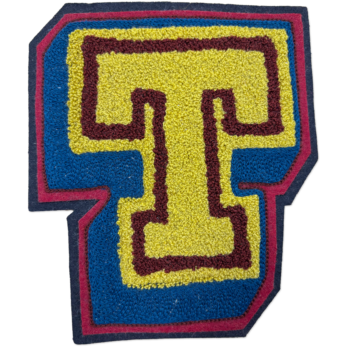 A hand-made chainstitch patch shaped like the letter T, featuring a yellow center with a dark burgundy outline, surrounded by a blue border and a dark navy outer edge.