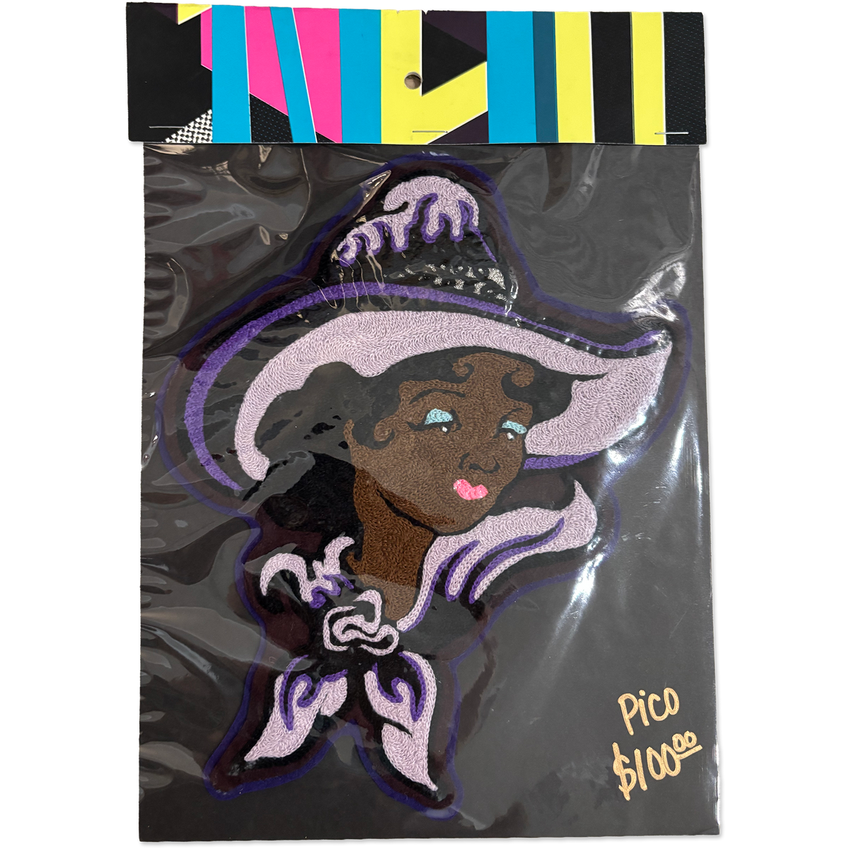 A packaged embroidered patch featuring a stylized witch character with a large lavender hat, dark hair, and purple trim, sealed in clear plastic with a colorful striped header card. Handwritten text in the corner reads 'Pico $100€'.