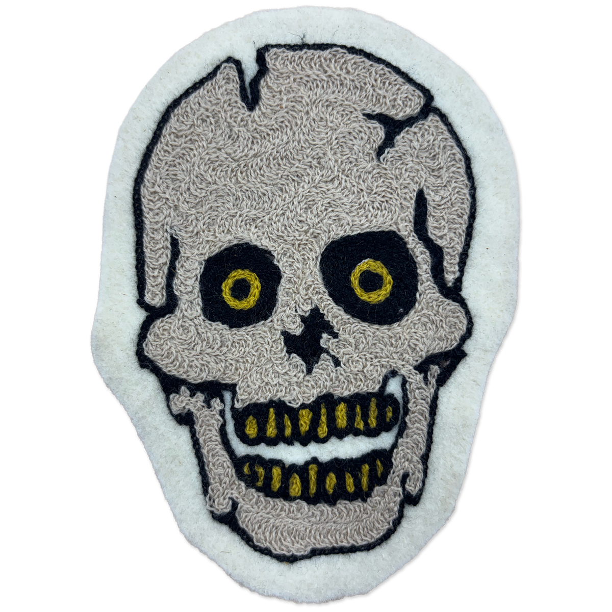 A skull-shaped embroidered patch with a textured beige skull design, black outlines, and yellow details on a white felt background.