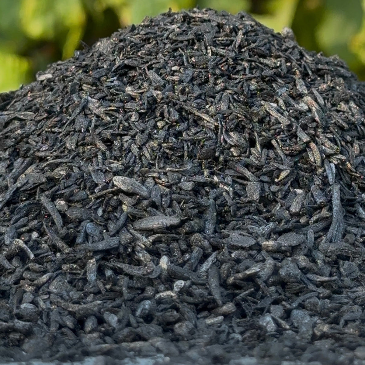 A close-up pile of dark, charred plant material, with a soft green blurred background.